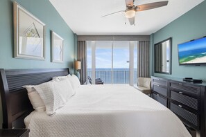 A hotel room with a bed, a ceiling fan, a television, and a view of the ocean through the window. - Lighthouse 1505 by Liquid Life (Gulf Shores)
