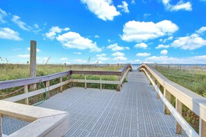 A wooden boardwalk leading to a beach with a clear sky. - Lighthouse 1505 by Liquid Life (Gulf Shores)