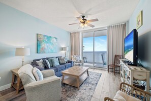 Un salón con sofá, sillones, una mesa de centro, televisor y un balcón con vistas.