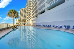 A swimming pool with lounge chairs, a palm tree, and a tall building in the background. - Lighthouse 716 by Liquid Life (Gulf Shores)