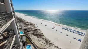 Blick auf den Strand vom Hotelbalkon mit Pool, Liegestühlen und Sonnenschirmen.