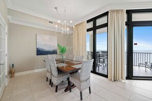 A dining area with a wooden table, wicker chairs, a chandelier, and a view of the balcony. - The Oasis at Orange Beach 1508 by Liquid Life (Orange Beach)