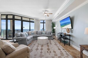 Ein geräumiges Wohnzimmer mit einem großen Ecksofa, einem runden Couchtisch und einem an der Wand befestigten Fernseher.