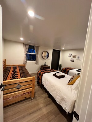 A compact hotel room with a wooden bed, a small bedside table, a mirror, and a window with curtains. - Newest Gem - Apache Oaks in Patagonia, AZ (Santa Cruz County)