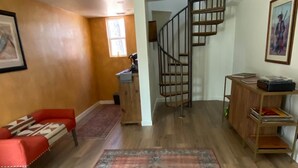 A spacious living area with a wooden floor, a red sofa, a patterned rug, a staircase, and a wooden cabinet.