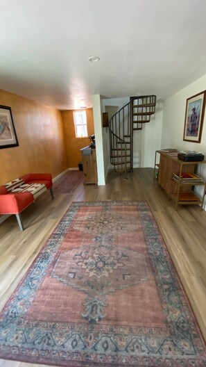 Ein geräumiger Wohnbereich mit Holzboden, einem roten Sofa, einem gemusterten Teppich, einer Treppe und einem Holzschrank.