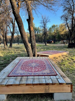 A wooden deck with a patterned rug, surrounded by trees in a natural setting.