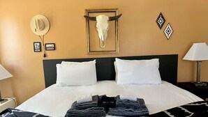 A hotel room with a bed, a headboard, a wall-mounted cow skull, framed pictures, and a lamp. - Apache Oaks in Patagonia, AZ (Santa Cruz County)