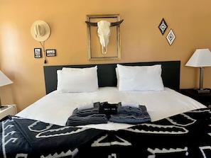 A hotel room with a bed, a headboard, a wall-mounted cow skull, framed pictures, and a lamp.