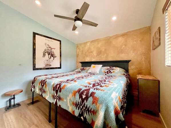 A bedroom with a bed, a ceiling fan, a framed picture on the wall, and a small table.