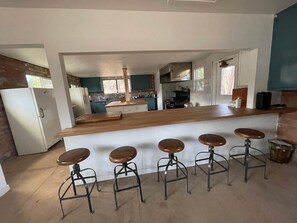 Una cocina con una isla central, taburetes de bar y un refrigerador.