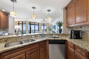 A modern kitchen with granite countertops, wooden cabinets, a stainless steel dishwasher, and a coffee maker. - The Oasis at Orange Beach 710 by Liquid Life (Orange Beach)
