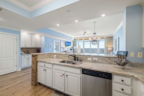 A modern kitchen with white cabinetry, a marble countertop, and a dishwasher. - Phoenix Orange Beach 1805 by Liquid Life (Orange Beach)