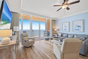 A spacious living room with a large window overlooking the sea, a ceiling fan, and a sofa set. - Phoenix Orange Beach 1805 by Liquid Life (Orange Beach)