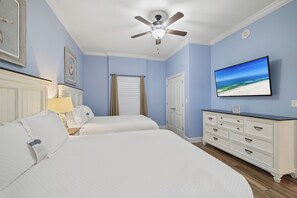 Un dormitorio con dos camas, un ventilador de techo, un televisor en la pared y un aparador.