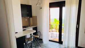 A compact kitchen with a dining area, a heart-shaped towel on the bed, and a view of greenery outside. - Casale Regina - Marina di Camerota (Marina di Camerota)