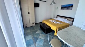 A hotel room with a bed, a wardrobe, a desk with a chair, a small table, and a wall-mounted air conditioner. - Casale Regina - Marina di Camerota (Marina di Camerota)
