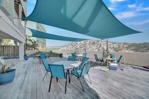 Eine Holzterrasse mit Gartenmöbeln, darunter ein Tisch und Stühle, beschattet durch ein großes Sonnensegel.