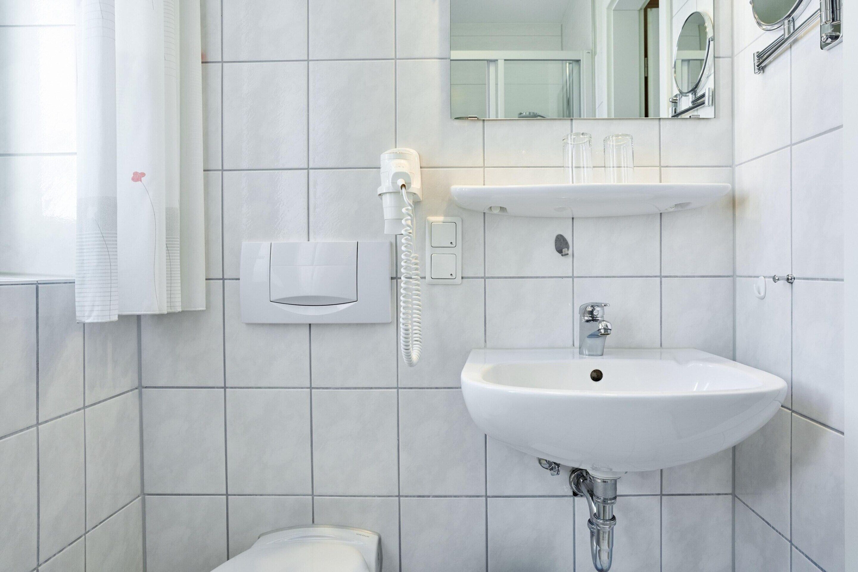 Un bagno con un lavandino bianco, uno specchio, un erogatore di asciugamani e un water.
