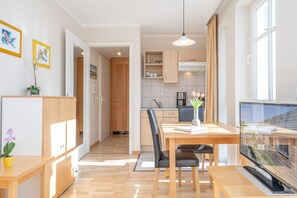 Eine moderne Küche mit Holzschränken, ein Essbereich mit Tisch und Stühlen sowie ein an der Wand montierter Fernseher.