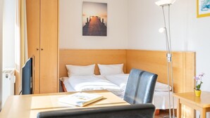Hotellihuone, jossa on sänky, työpöytä, tuoli, yöpöytä lampun kanssa, vaatekaappi ja seinällä oleva kehystetty kuva.