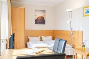Ein Hotelzimmer mit Bett, Schreibtisch, Stuhl, Nachttisch mit Lampe, Kleiderschrank und einem gerahmten Bild an der Wand.