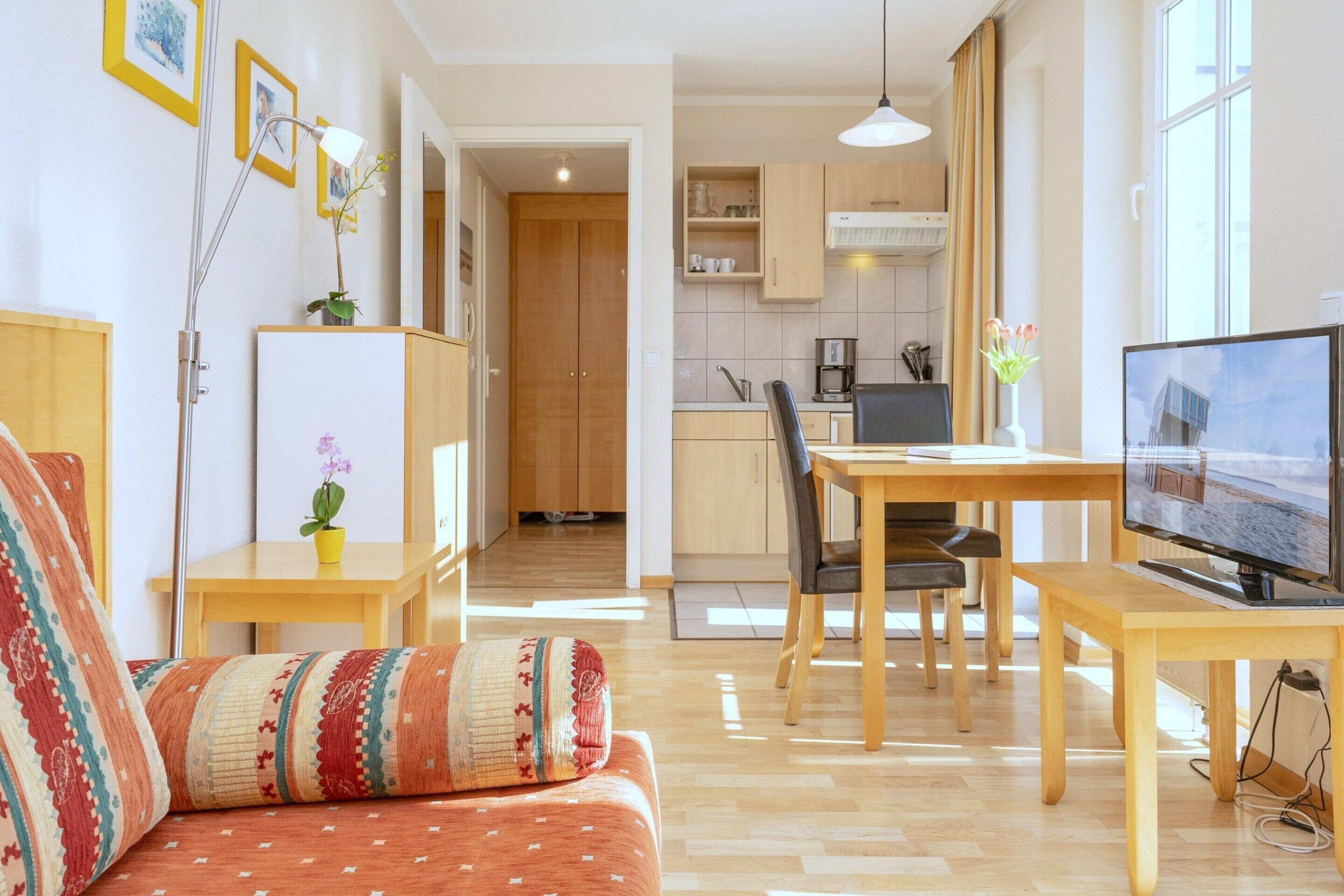 A living room with a sofa, a TV, a dining table, and a kitchen in the background.