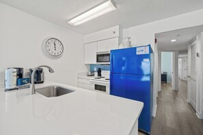 Eine moderne Küche mit einer Edelstahl-Spüle, einem blauen Kühlschrank und einer Wanduhr.