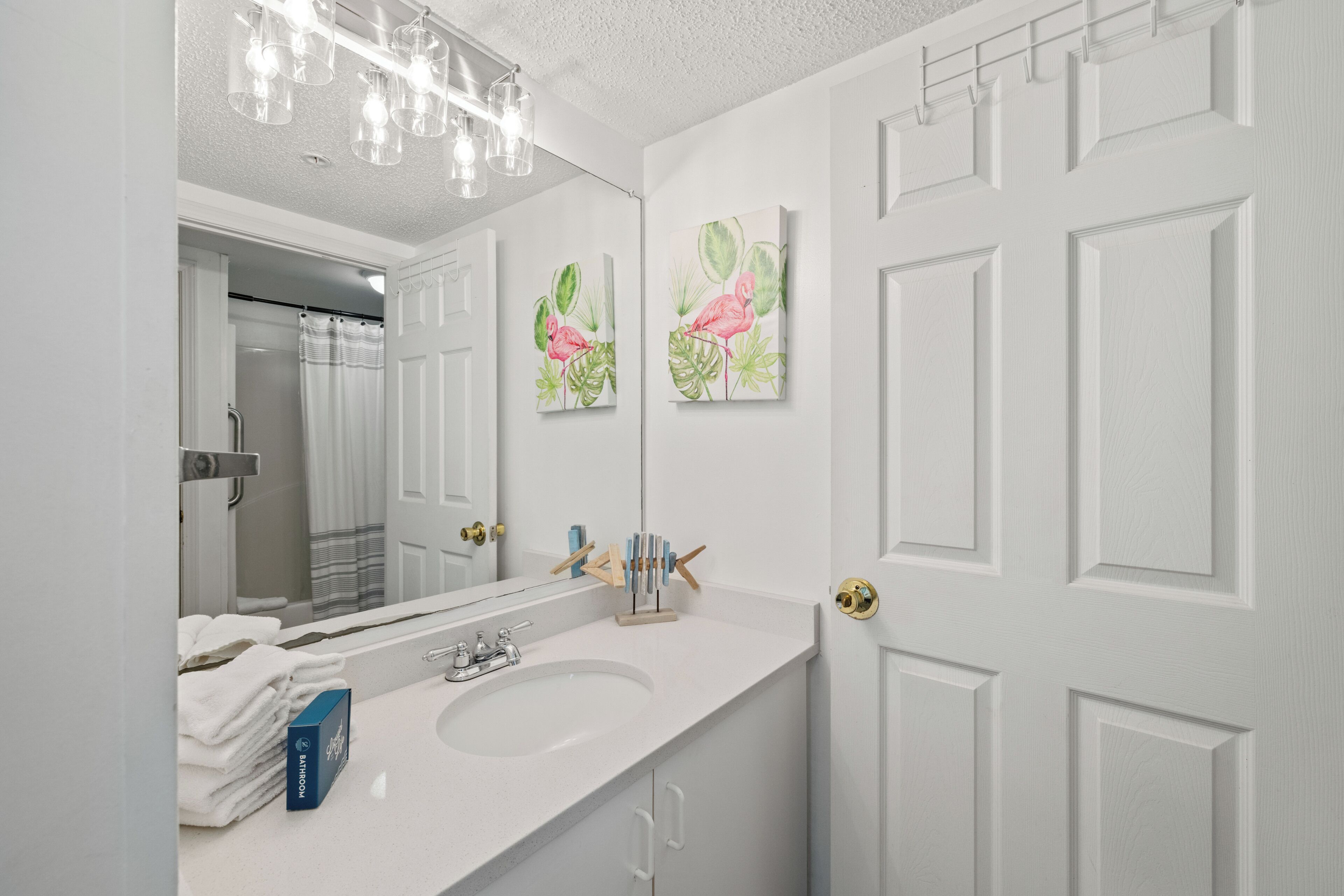 A bathroom with a white sink, a mirror, and two wall-mounted paintings of flamingos.