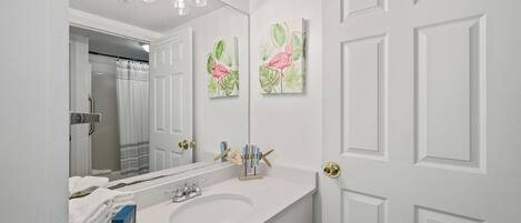 A bathroom with a white sink, a mirror, and two wall-mounted paintings of flamingos.