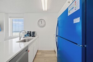 Eine moderne Küche mit weißer Arbeitsplatte, einer Edelstahl-Spüle, einer Kaffeemaschine, einer Uhr und einem blauen Kühlschrank.
