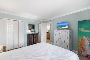 A bedroom with a large bed, a television on a cabinet, and a door leading to another room. - Romar Tower 3B by Liquid Life (Orange Beach)