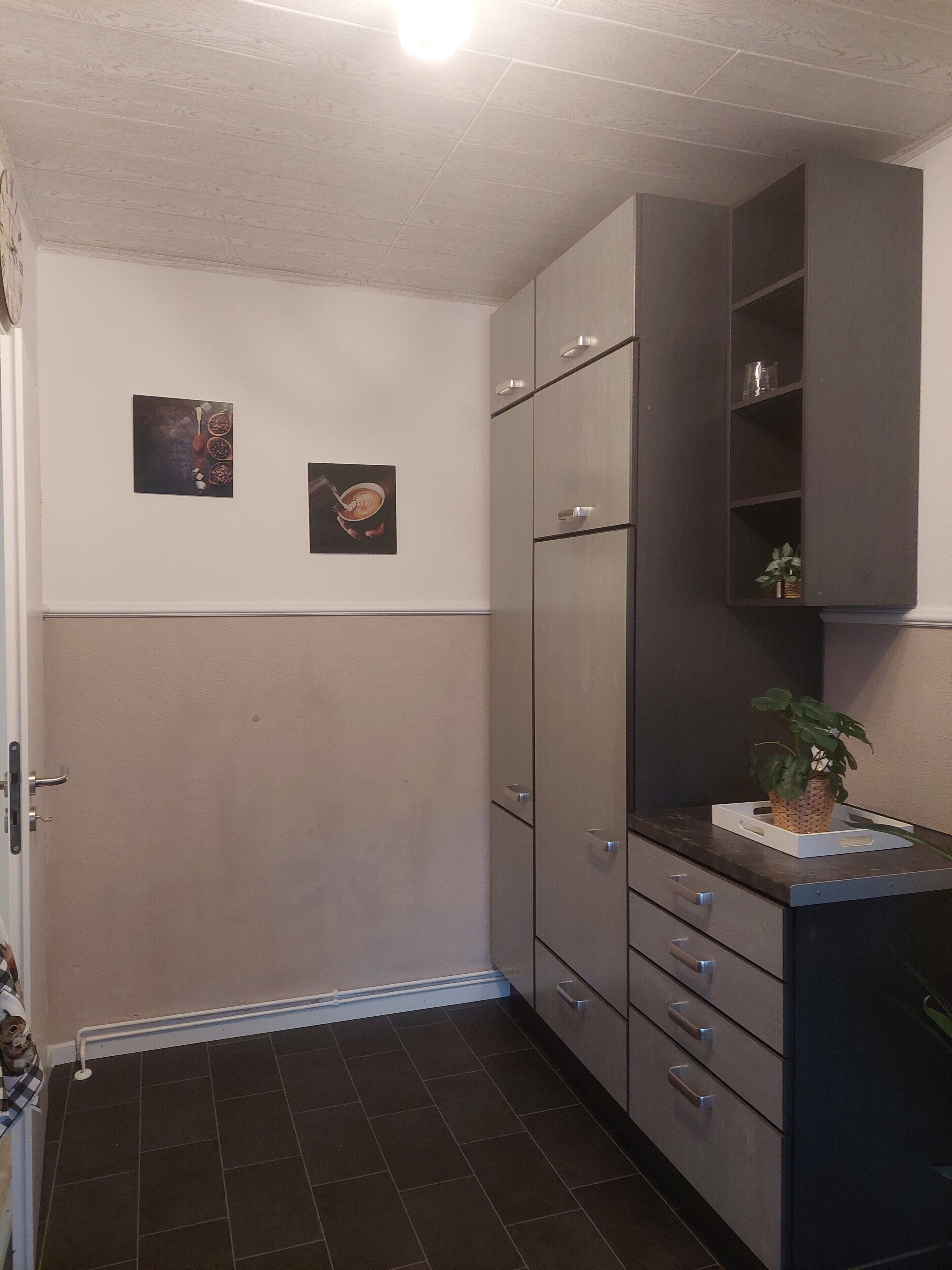 Une cuisine avec des carreaux de couleur sombre, une porte blanche et deux tableaux encadrés accrochés au mur.
