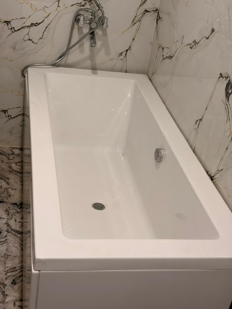 A white bathtub with a showerhead and faucet, set against a marble wall.