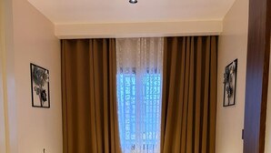 Ein Zimmer mit einer Couch, einem Holztisch, einem Fenster mit Vorhängen und gerahmten Bildern an den Wänden.