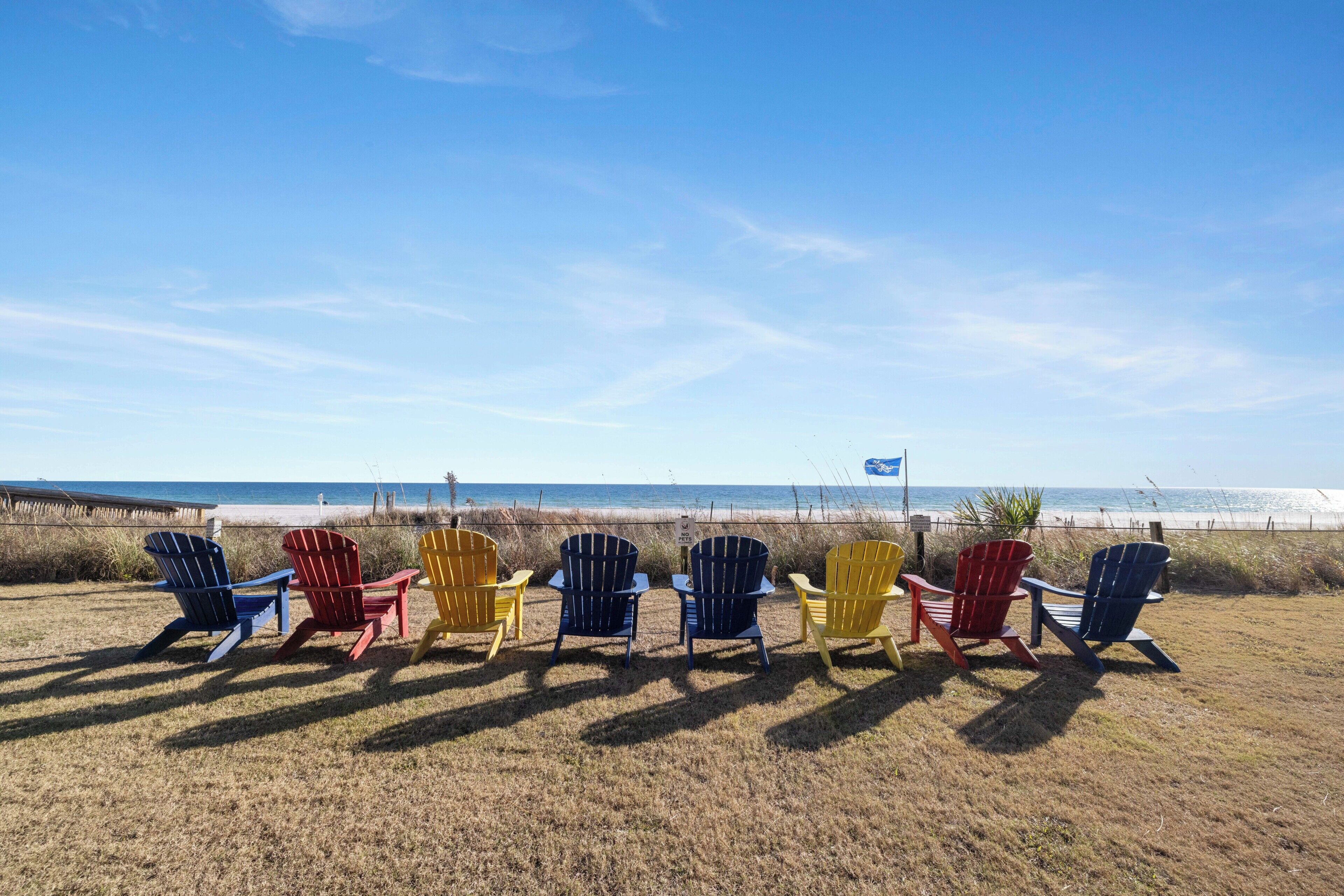 Eine Reihe bunter Adirondack-Stühle, die auf einen Strand mit blauem Himmel ausgerichtet sind.