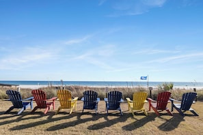 Eine Reihe bunter Adirondack-Stühle mit Blick auf einen Strand und einen klaren Himmel.