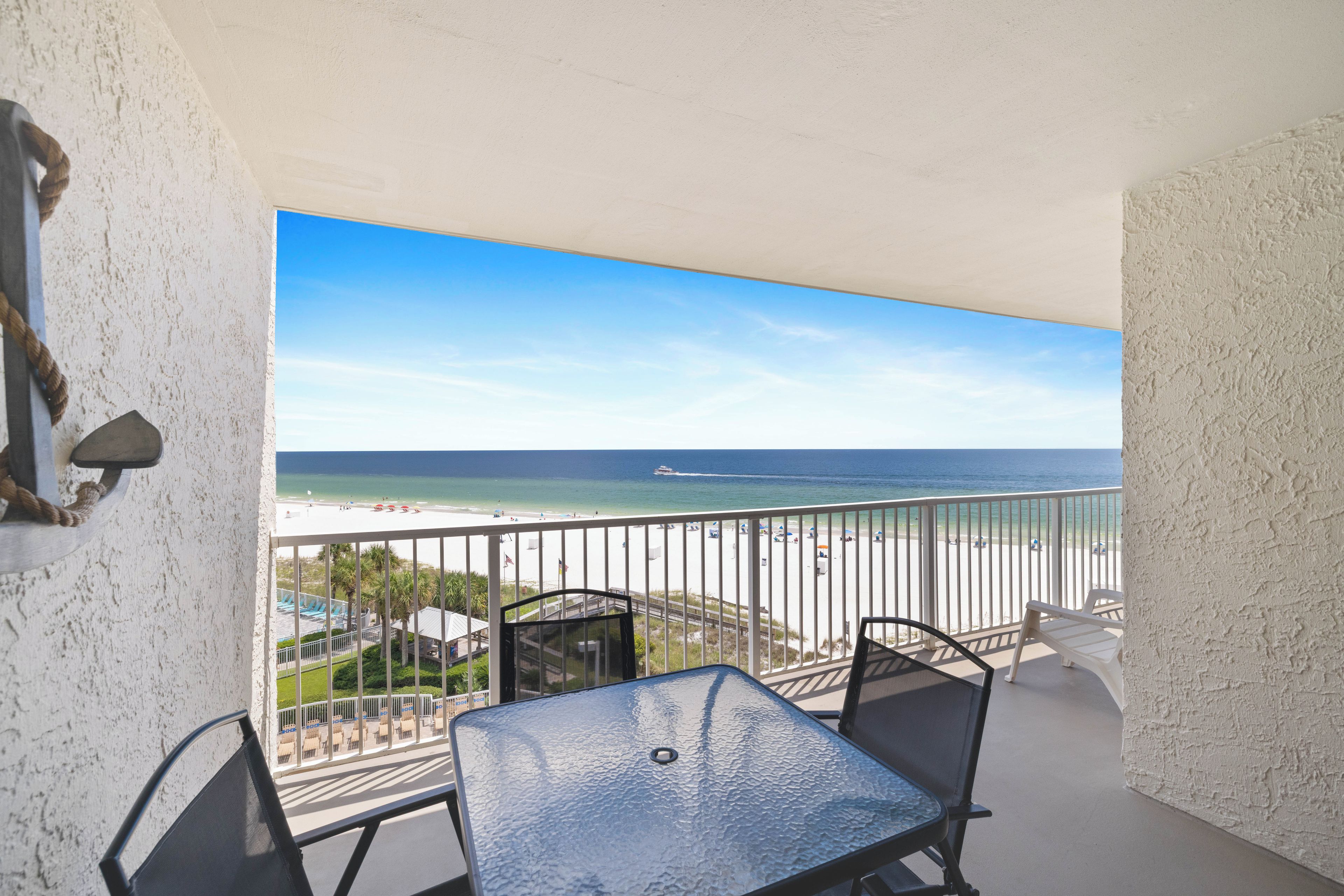 A balcony with a table and chairs, overlooking a beach with umbrellas and a clear view of the ocean.