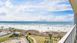 Blick auf den Strand vom Balkon aus, mit Pool und Liegestühlen.