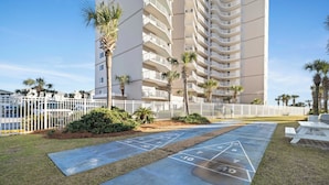 A courtyard with a shuffleboard court, palm trees, and a white fence. - Seaside Beach & Racquet 4608 by Liquid Life (Orange Beach)