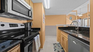 Una cocina compacta equipada con microondas, estufa, cafetera, lavaplatos y fregadero.