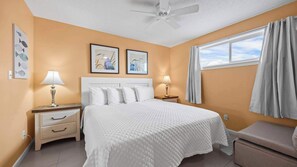 A hotel room with a bed, two bedside tables with lamps, a ceiling fan, artwork on the walls, and a window with curtains. - Sugar Beach 325 by Liquid Life (Orange Beach)
