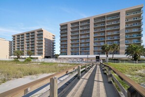 A beachfront hotel with multiple balconies, a pool area, and a wooden boardwalk leading to the entrance. - Surfside Shores 1803 by Liquid Life (Gulf Shores)
