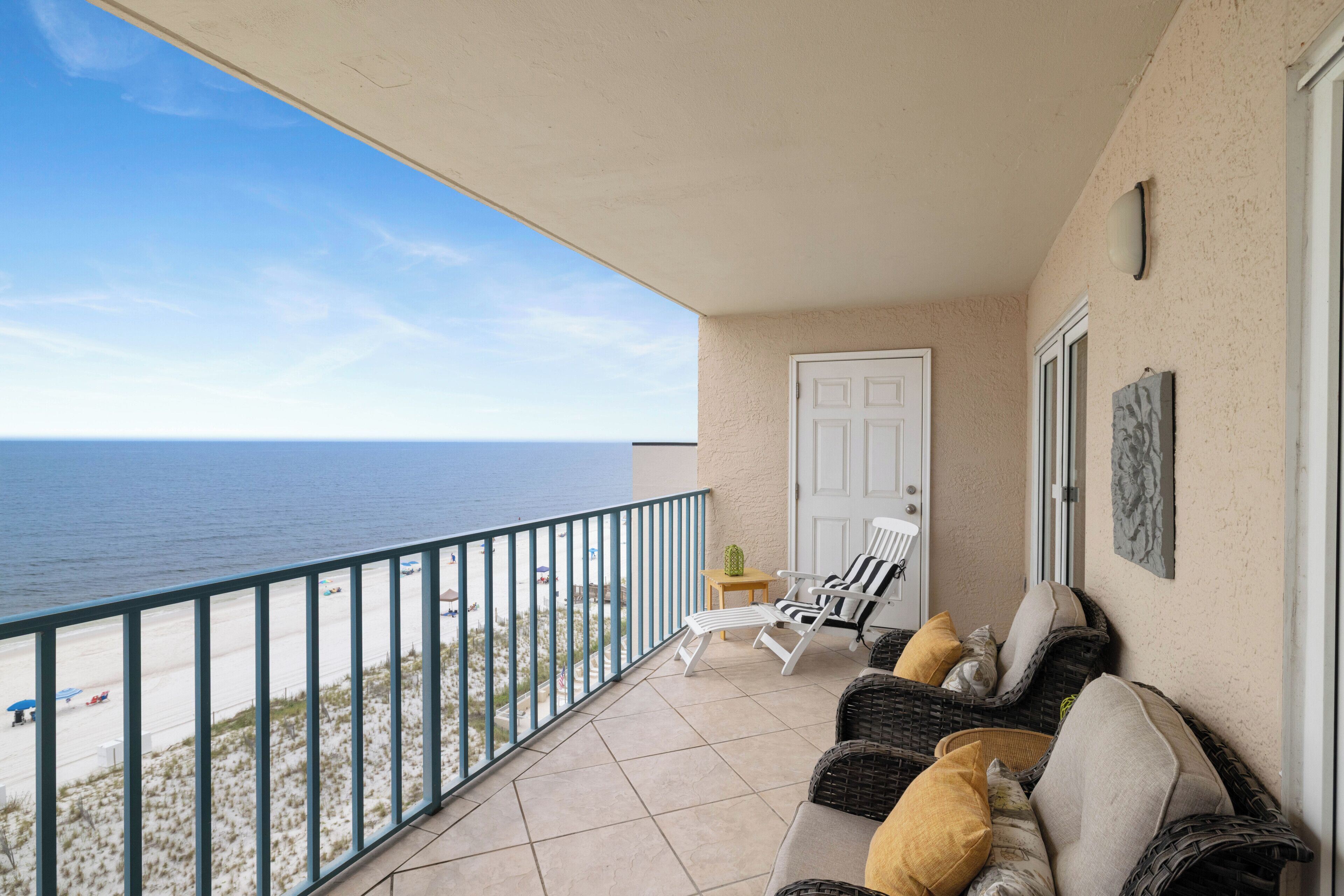 A balcony with a view of the ocean, a white door, and wicker furniture.