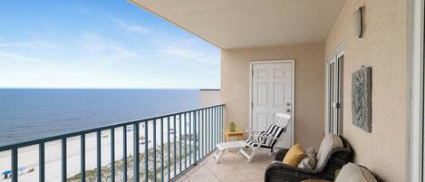 Un balcon avec vue sur l’océan, une porte blanche et des meubles en osier.