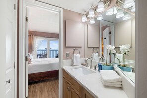 Ein Badezimmer in einem Hotel, ausgestattet mit einem großen Spiegel, einem Waschbecken und einer Toilette. Ein Fenster mit Vorhängen bietet einen Blick nach draußen.