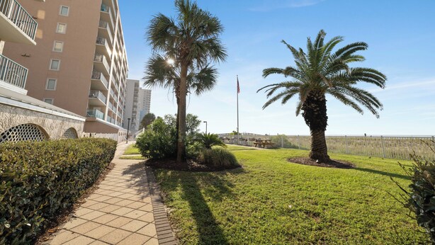 A pathway leading to a building with multiple balconies, surrounded by well-maintained grass and palm trees. - Surfside Shores 1803 by Liquid Life (Gulf Shores)