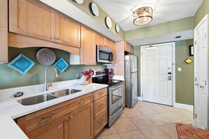 A kitchen with wooden cabinets, stainless steel appliances, and a white countertop. - Surfside Shores 1803 by Liquid Life (Gulf Shores)