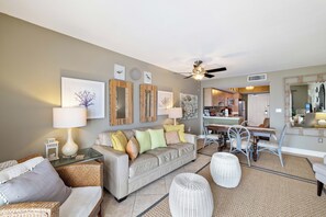 A living room with a sofa, chairs, a dining table, and a kitchen in the background. - Surfside Shores 1803 by Liquid Life (Gulf Shores)