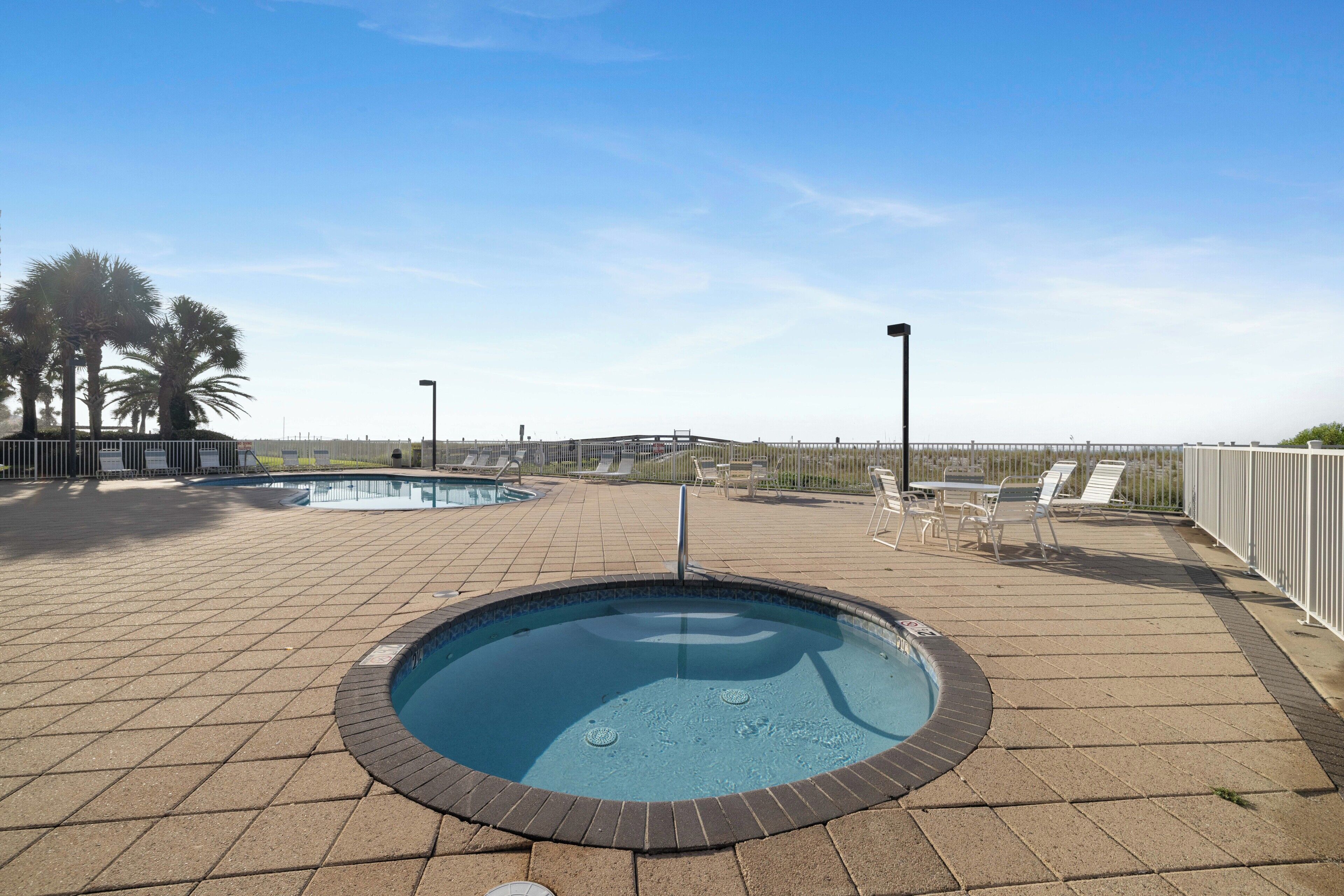 A rooftop pool area with a hot tub, lounge chairs, and a view of the city skyline.